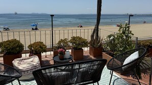 Un balcón con mobiliario exterior, plantas en macetas y vistas a la playa y al mar.
