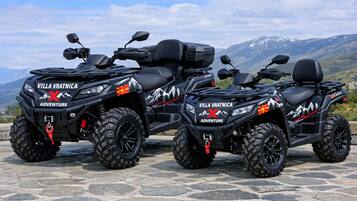Trois quads arborant le logo « Villa Vratnica Adventure » sont stationnés sur une surface en pierre, avec une chaîne de montagnes en arrière-plan.