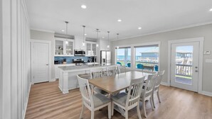 Una cocina amplia con una isla central, armarios blancos y una zona de comedor con una mesa y sillas de madera.