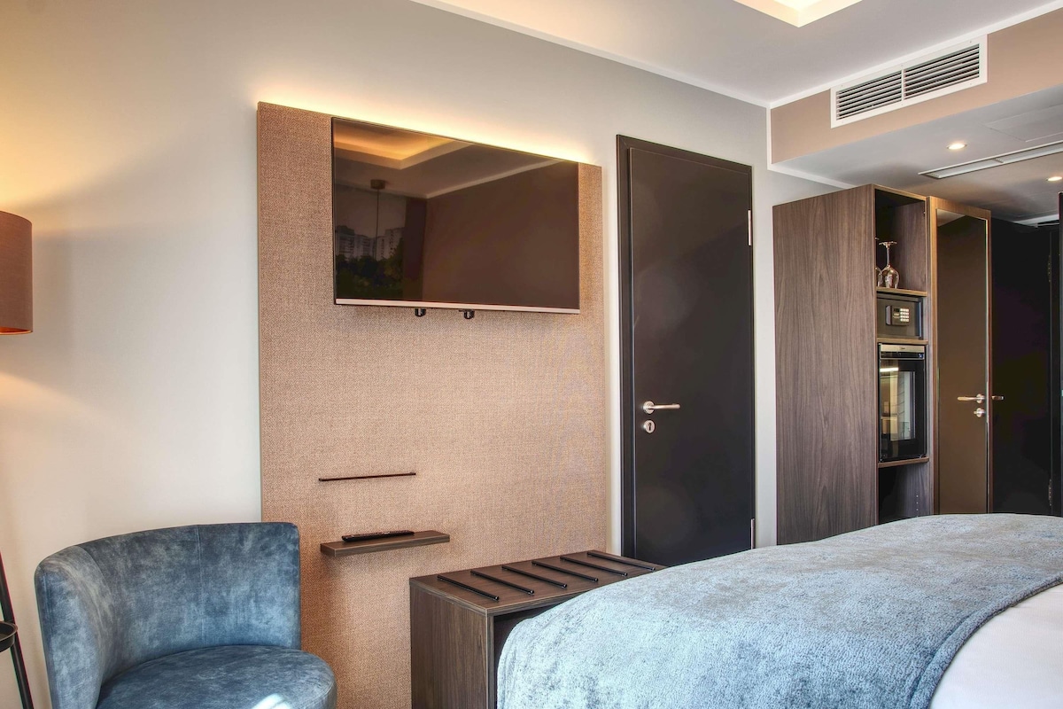 Ein modernes Hotelzimmer mit einem Bett, einer Sitzecke, einem Kleiderschrank und einem Spiegel.