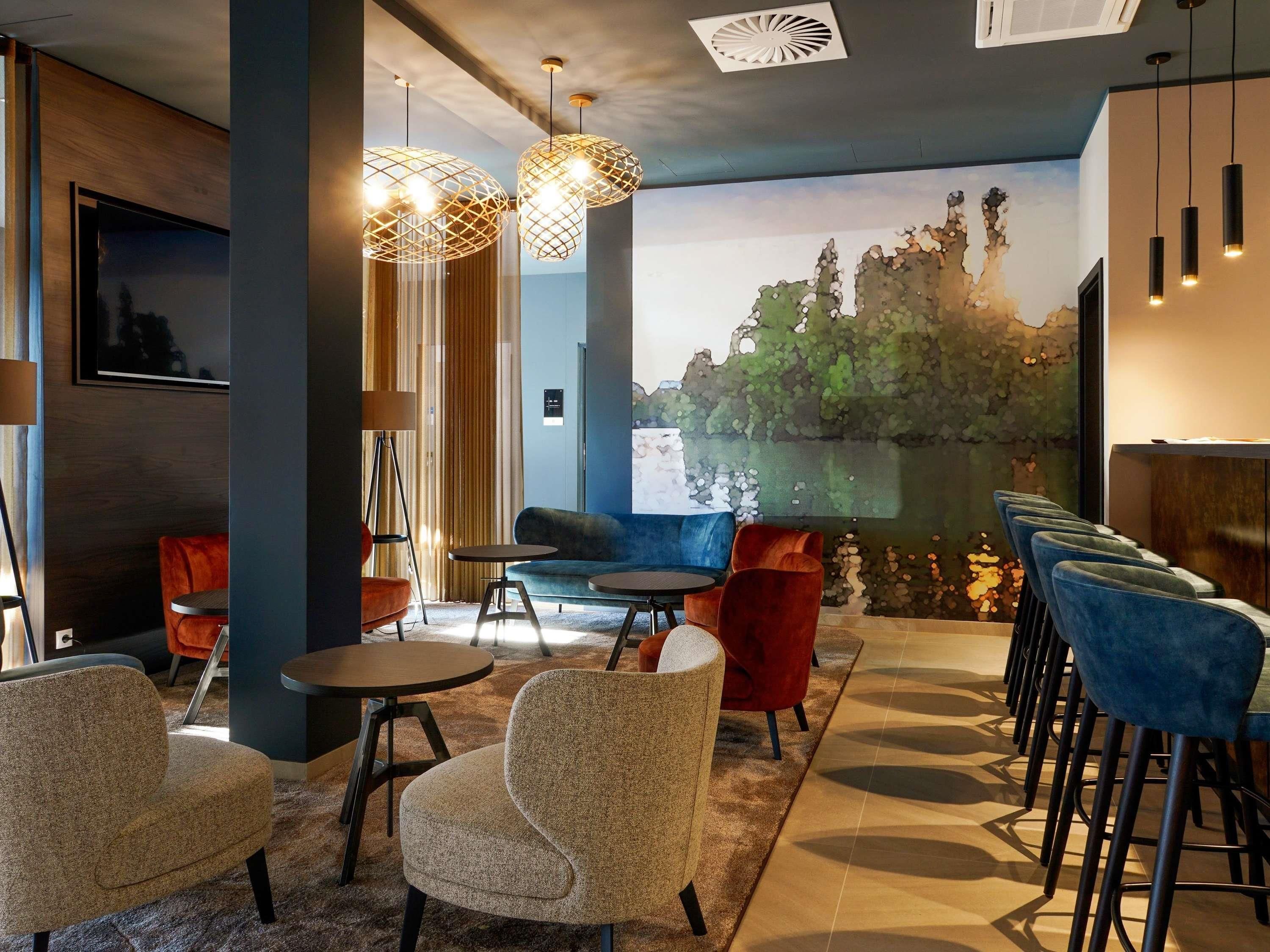 Uma área de estar moderna com vista para um lago, apresentando um bar com banquetas altas, um sofá e cadeiras estampadas.