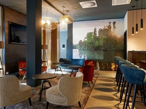 Un área de descanso moderna con vista a un lago, que incluye un bar con taburetes altos, un sofá y sillones estampados.