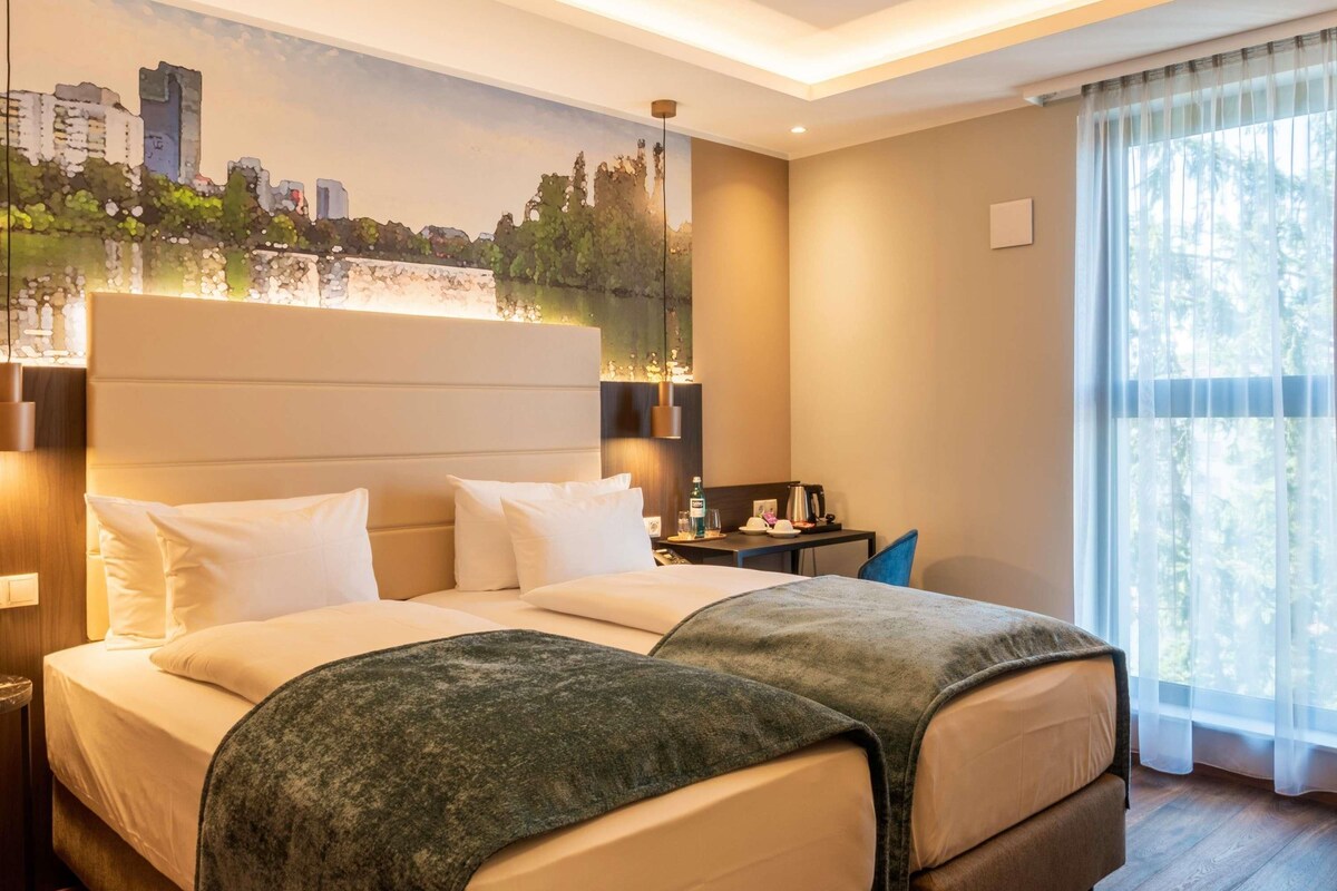 Ein Hotelzimmer mit einem großen Bett, einem Schreibtisch, einem Sessel, einem Nachttisch und einer Wandmalerei mit Stadtansicht.