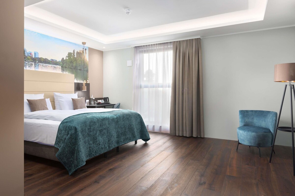 Ein Hotelzimmer mit Bett, Schreibtisch, Stuhl, Lampe und Blick auf die Stadt.