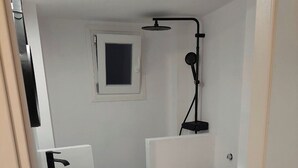 Une petite salle de bain avec un lavabo, des toilettes et une douche, le tout de couleur blanche.