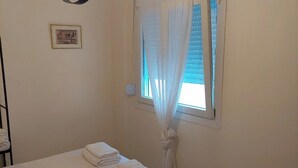 Une chambre à coucher avec un lit, une fenêtre ornée de rideaux légers, un tableau accroché au mur et un luminaire placé au-dessus du lit.