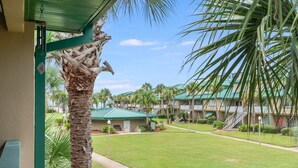 A hotel courtyard with a green lawn, palm trees, and a building with a green roof.