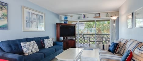 Una sala de estar con un sofá azul, un sofá a rayas, una mesa de centro blanca y un televisor sobre un mueble de madera.