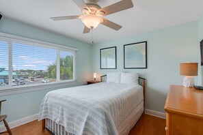 A bedroom with a bed, a ceiling fan, a nightstand, a lamp, and a window with blinds. - Seaspray Condos - 102D (Fort Walton Beach)