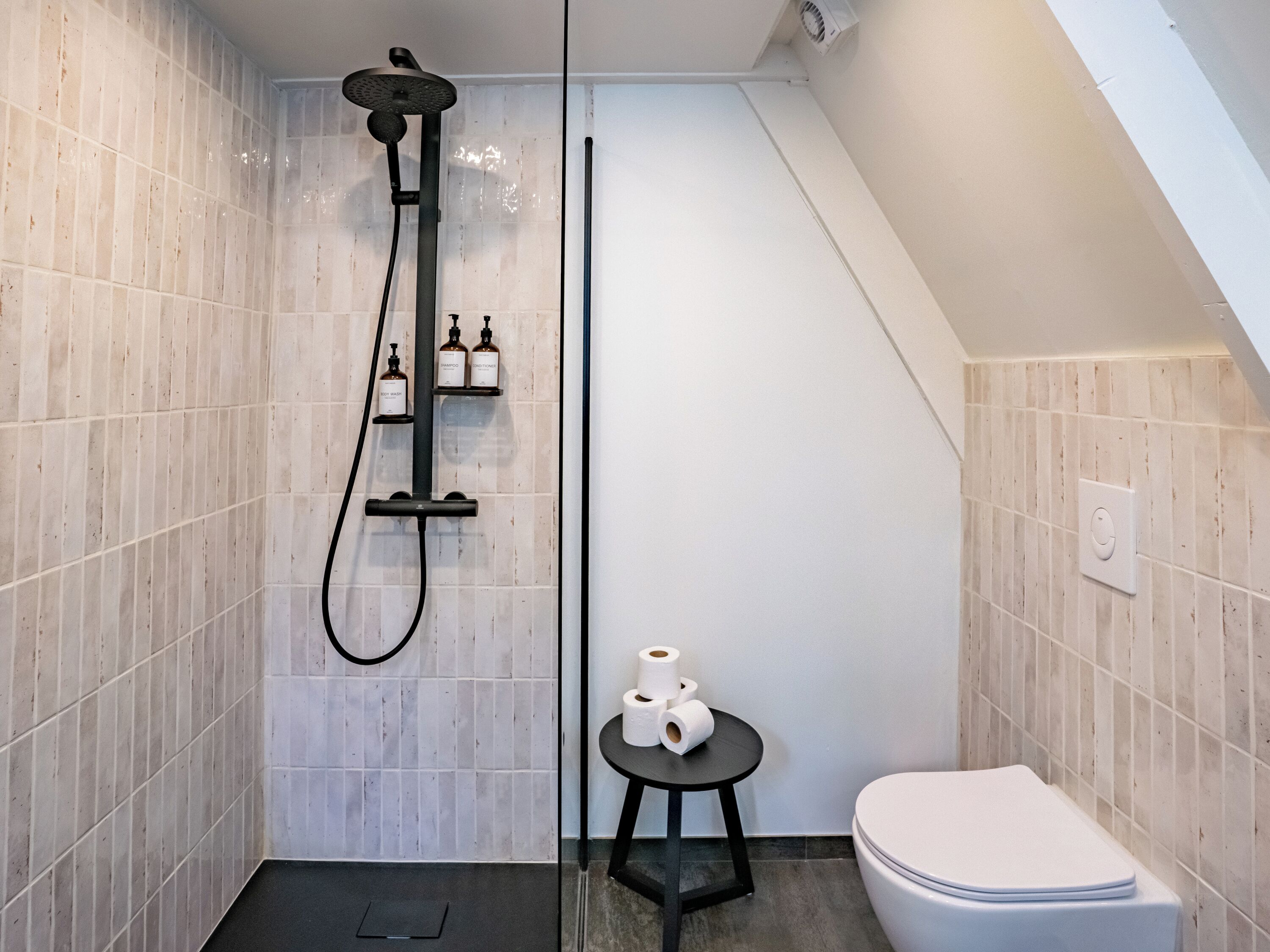 Ein modernes Badezimmer mit Dusche, Toilette und einem kleinen Tisch mit Pflegeprodukten.
