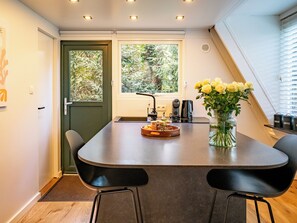 A modern kitchen with a central island, two black chairs, a vase of yellow flowers, and a window with a view of greenery. - Boshuisje Rekem One-Bedroom Houses (Lanaken)