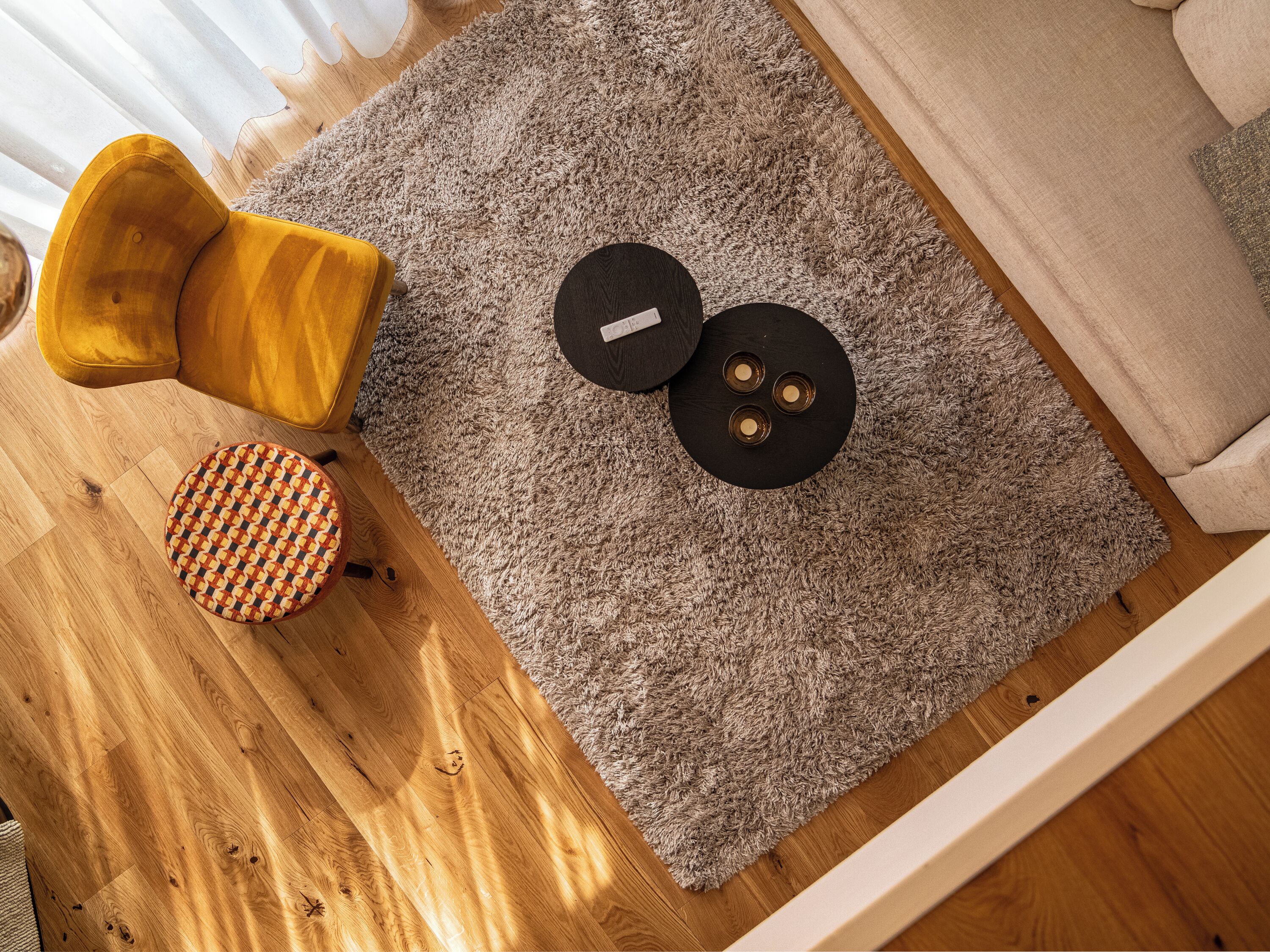 A room with a wooden floor, a grey shaggy rug, a yellow armchair, a round ottoman, and a black circular object on the rug.