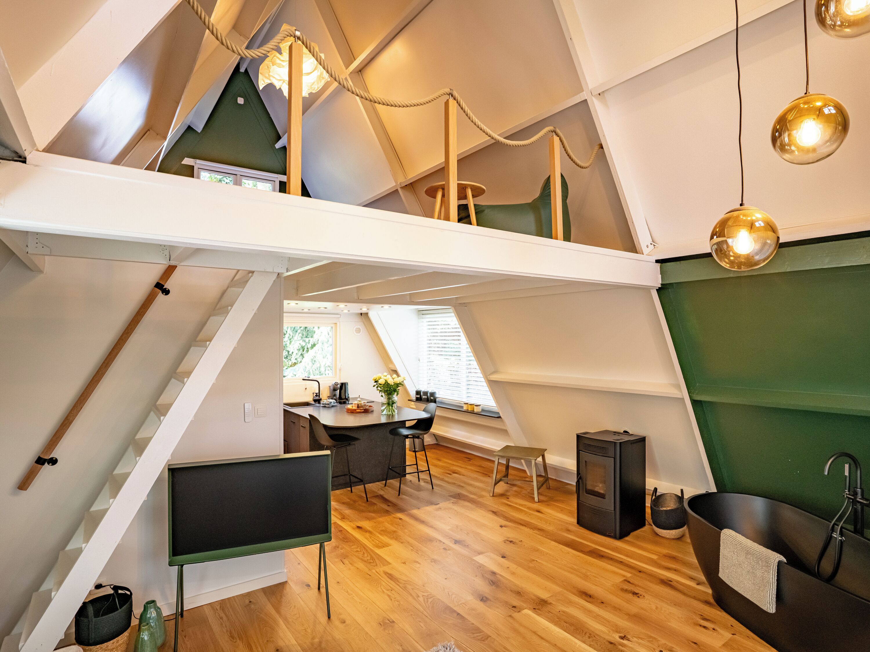 A modern loft-style room with a kitchen, dining area, and a large black bathtub.