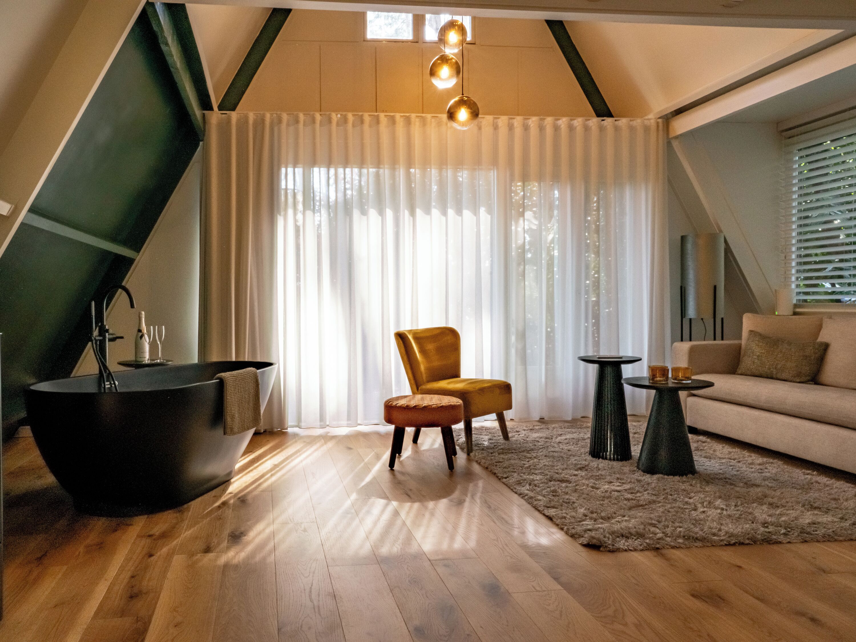 Un salón moderno con suelo de madera, una bañera negra, un sillón amarillo, un sofá beige y una pequeña mesa redonda.