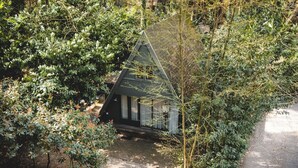 A small, dark-colored cabin surrounded by dense foliage, with a gravel path leading to it. - Boshuisje Rekem One-Bedroom Houses (Lanaken)