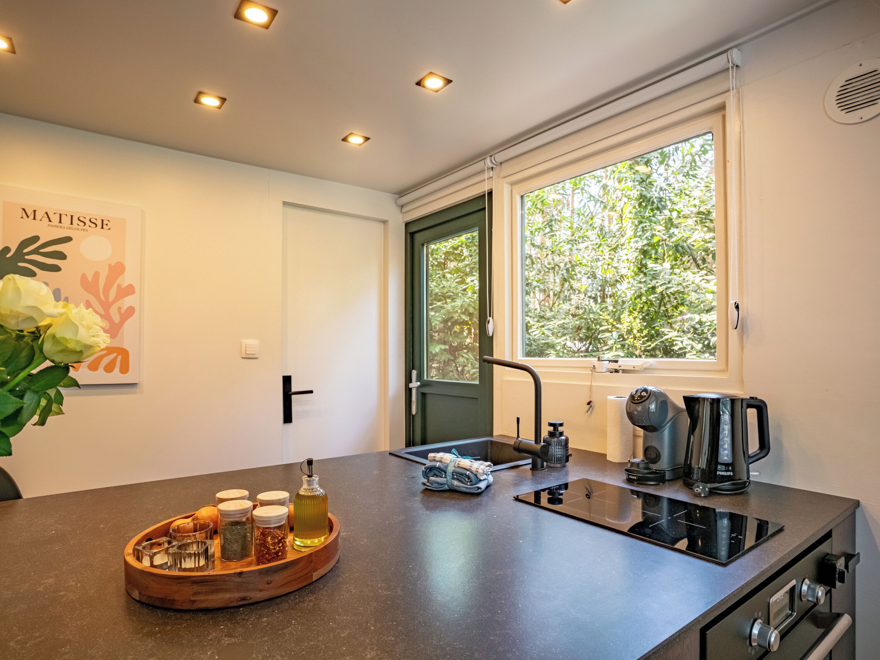 A modern kitchen with a black countertop, a built-in stove, a sink, and a window with a view of greenery.