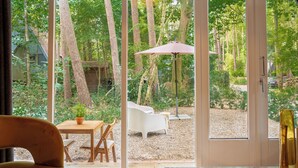 A room with a large sliding glass door leading to an outdoor patio with a wooden table, a white chair, and a patio umbrella. - Boshuisje Rekem One-Bedroom Houses (Lanaken)