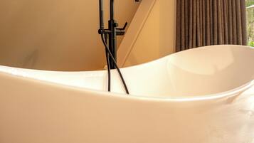 A modern bathtub with a black faucet and hose, beige walls, and a window with curtains.
