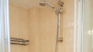 Een douchecabine met glazen wanden, een handdouche en een wandmengkraan.