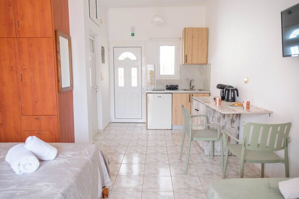 Una habitación de hotel con cama, una kitchenette pequeña y un comedor con sillas.