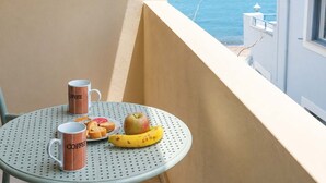 Een balkon met een tafel gedekt voor het ontbijt, inclusief koffiemokken, een banaan, een appel en gebak.