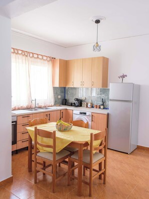 Una cuina compacta amb armaris de fusta, taula de dinar amb cadires, nevera i rentadora.