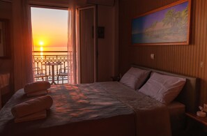 Une chambre d’hôtel avec un lit, un tableau accroché au mur et une vue sur le coucher de soleil, visible à travers la porte du balcon.
