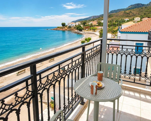A balcony with a table and chairs overlooking a beach and sea.