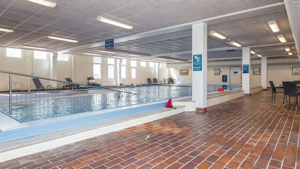 Ein Hallenbad mit Fliesenboden, transparenter Decke und Beleuchtung sowie einigen Schwimmenden.