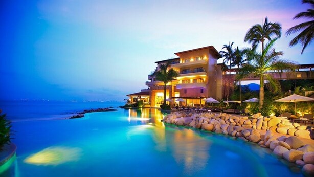 A resort with a large infinity pool, a multi-story building, and palm trees.
