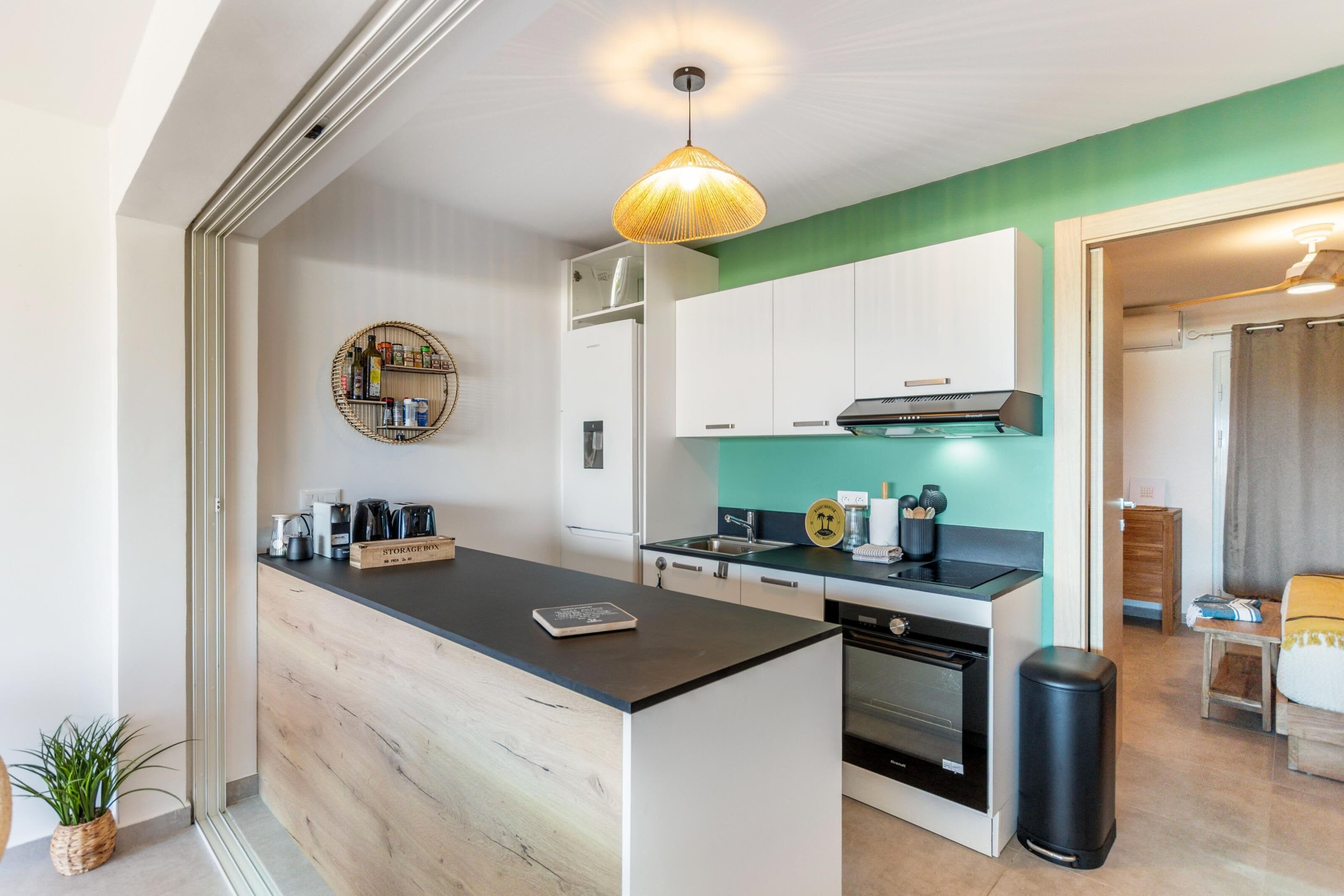 A modern kitchen with white cabinets, a black countertop, and a hanging light fixture.