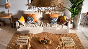 A cozy living room with a sofa, two wooden stools, a round coffee table, and a woven rug.