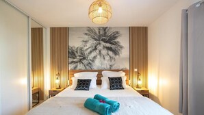 A hotel room with a large bed, two bedside tables with lamps, a wall-mounted artwork of palm trees, and a ceiling light fixture.
