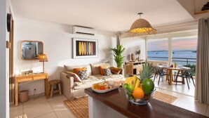 A modern living room with a sofa, dining table, and a view of the sea.
