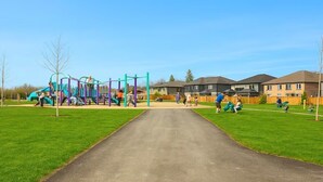 A playground with various play structures and a paved path leading to residential buildings. - Wasaga Luxury Coastal Escape (Wasaga Beach)