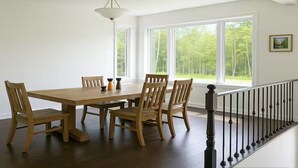 A dining area with a wooden table and chairs, large windows, and a staircase with a black railing. - Wasaga Luxury Coastal Escape (Wasaga Beach)