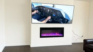 A living room with a mounted TV displaying a pilot's cockpit, a fireplace below the TV, and a dark wooden coffee table. - Wasaga Luxury Coastal Escape (Wasaga Beach)