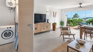 Ein modernes Wohnzimmer mit Waschmaschine, Holzmöbeln, einem Fernseher und Blick auf den Ozean.