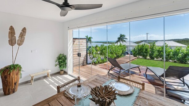 Ein geräumiger Balkon mit Holzterrasse, Deckenventilator und Blick auf das Meer und die Hügel.