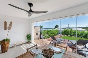A spacious balcony with a wooden deck, a ceiling fan, and a view of the sea and hills. - Griselles4  Sea view Heights Orient Bay  Unit 1BDR (SAINT MARTIN)