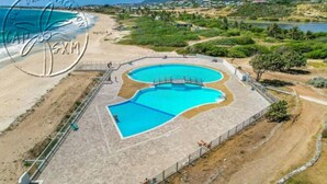 An aerial view of a resort with a large, irregularly shaped pool surrounded by a fence, a beach, and a hilly landscape in the background. - Serenity   Wonderful sea view   studio 4p (SAINT MARTIN)