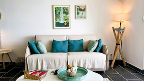 A living room with a striped sofa, teal cushions, a coffee table with a basket of fruits, and two framed artworks on the wall. - Serenity   Wonderful sea view   studio 4p (SAINT MARTIN)
