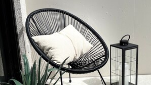 A black wicker chair with a cushion, a black lantern, and a potted plant on a tiled patio. - Modern Apartment in Ravensburg (Ravensburg)