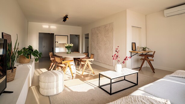 Un salon moderne avec une table à manger ronde, un canapé et une table basse. On y trouve également un téléviseur, une plante et un vase rempli de fleurs.