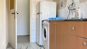 A compact kitchen with a washing machine, a refrigerator, and wooden cabinets.