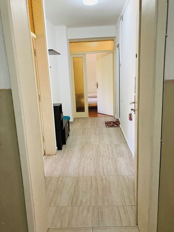 A hallway with a wooden floor leading to a room with a bed and a door with a keychain.