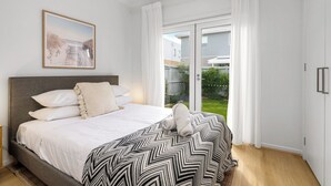 Ein Schlafzimmer mit einem Bett, einem Fenster mit Vorhängen, Blick ins Freie und einem Bild an der Wand.