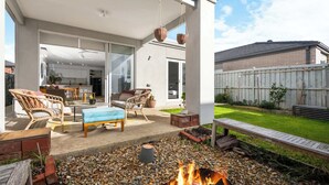 Eine überdachte Terrasse mit Korbmöbeln, einem Feuerkorb und Blick auf den Garten.