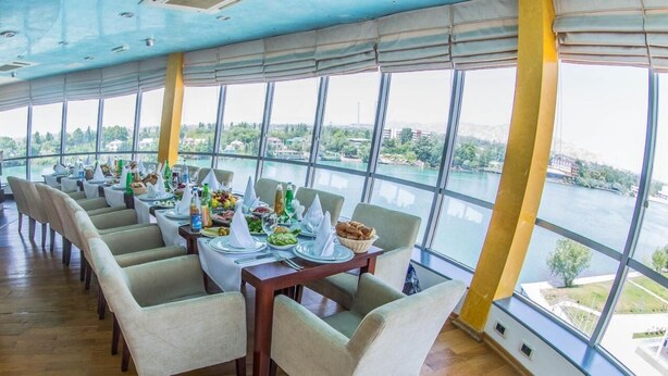 A restaurant with tables set for dining, large windows offering a view of a river and greenery. - Arena Hotel Kur (Mingacevir)