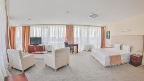 A hotel room with a bed, two armchairs, a TV, a desk, and a large window with curtains. - Arena Hotel Kur (Mingacevir)